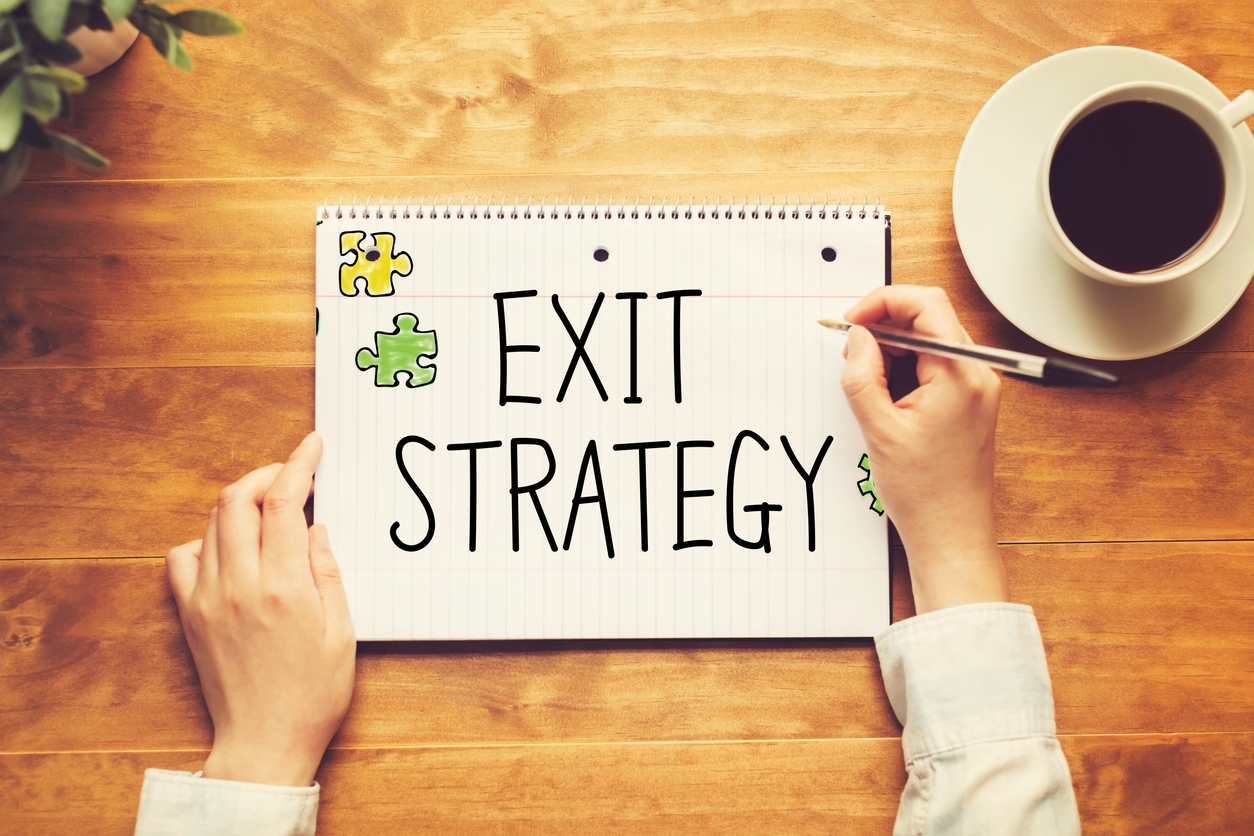 Person writing 'EXIT STRATEGY' on paper, to demonstrate exit planning concept