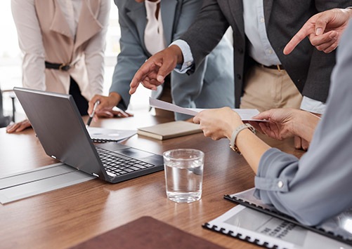 Hands, meeting and business people with a laptop and report for analysis, investment or trading. Discussion, computer and corporate employees at a desk for teamwork on financial analytics together