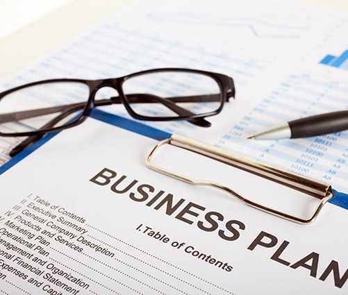 Detailed business plan document with charts, pen, glasses, and clipboard indicating preparation for investor visa citizenship by investment program.